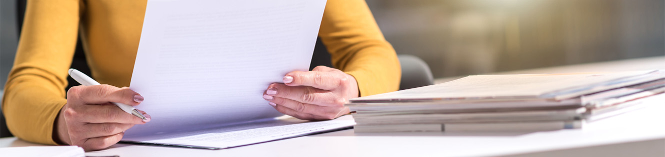 Woman sitting at desk holding pen and reading a paper