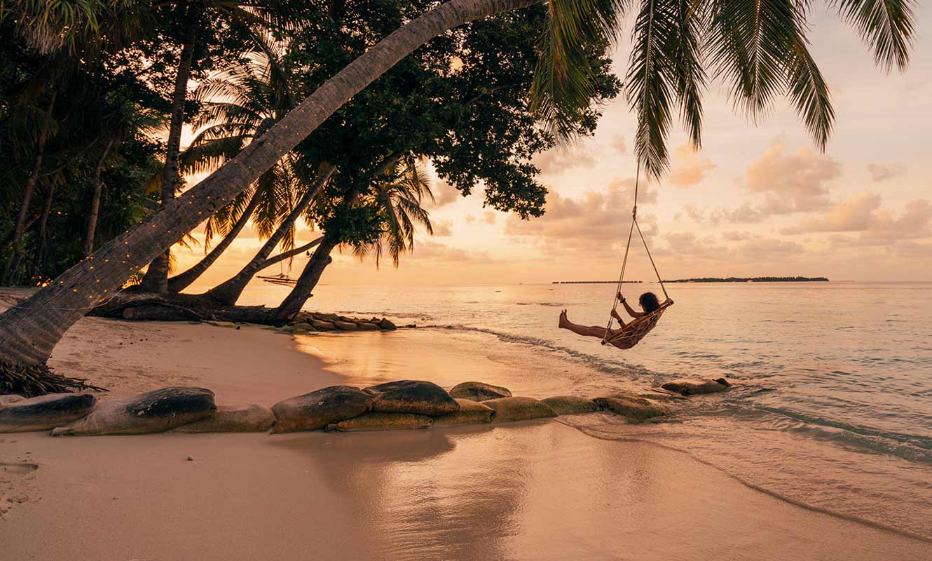 Woman relaxing in a swing at the beach watching sunset.