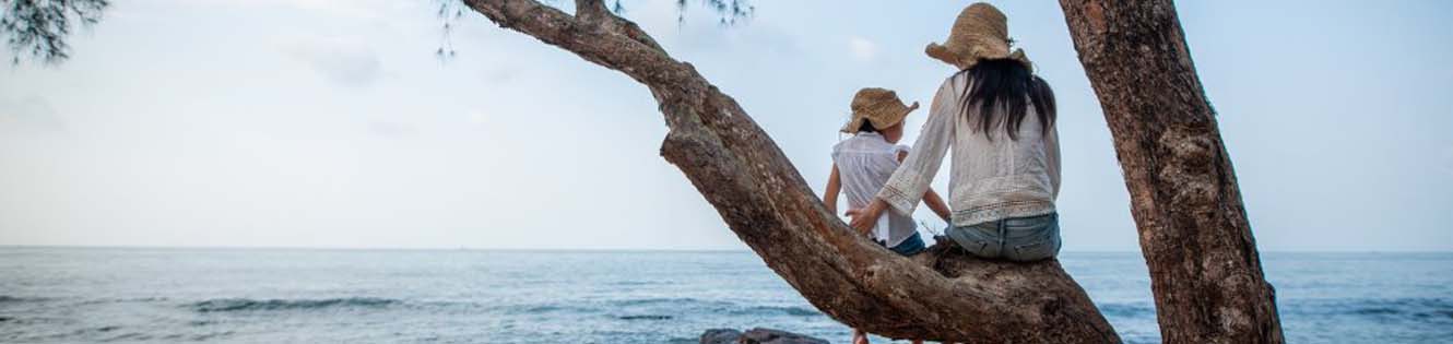 girls sitting on branch of tree near ocean