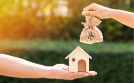 a hand holding a little house with a money bag hanging over it