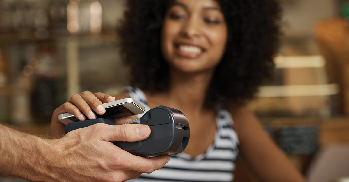 Woman holding phone over merchant device to use digital wallet